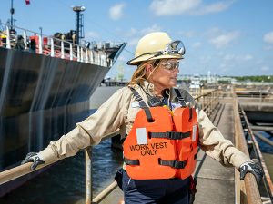 An employee wearing a hardhat and vest on the dock in a port